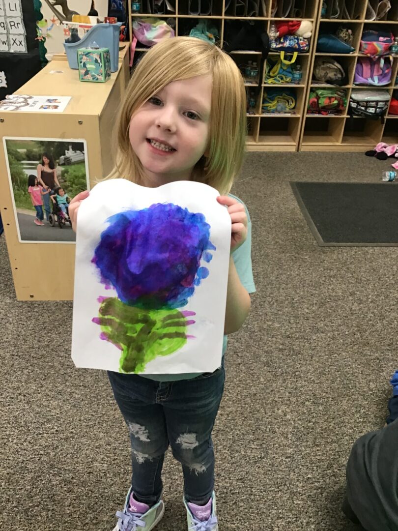 A little girl holding up a painting of flowers.